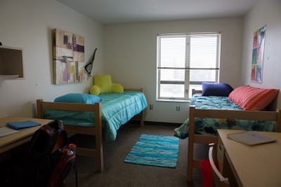 2 beds and 2 desks with a large window on the far wall.