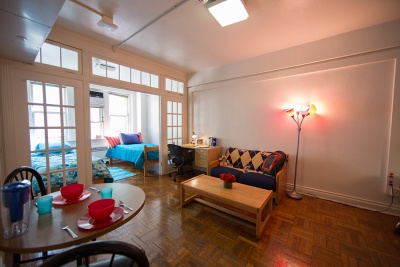 Wide angle shot of furnished bedroom, living, and dinging room space with a desk in the corner.