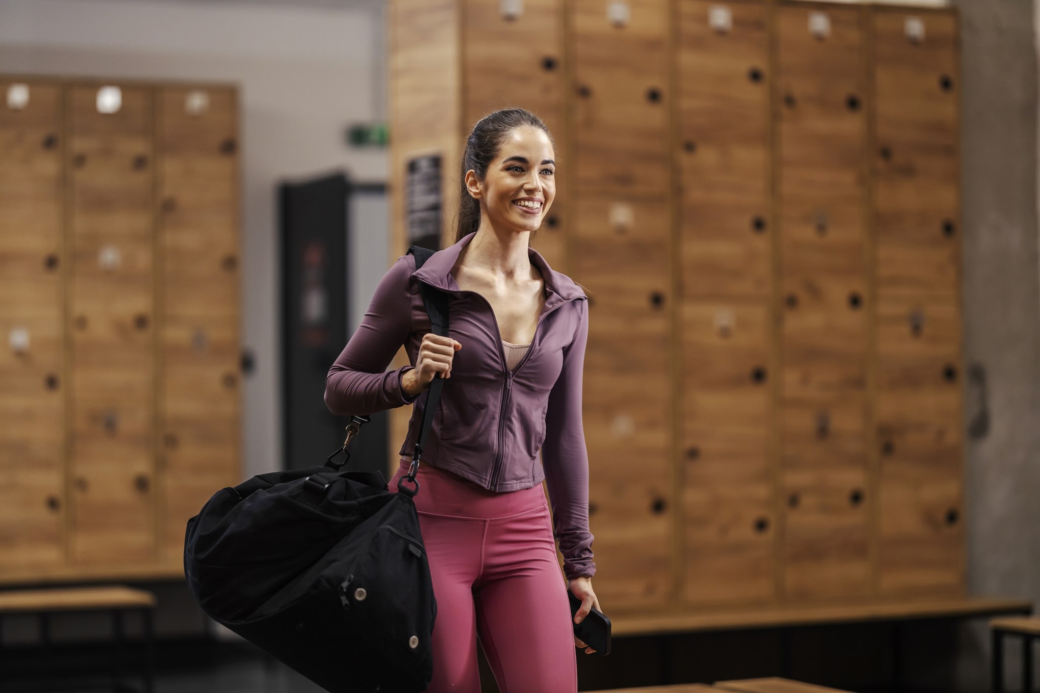 College student wearing workout clothes and holding a gym bag in a gym locker room