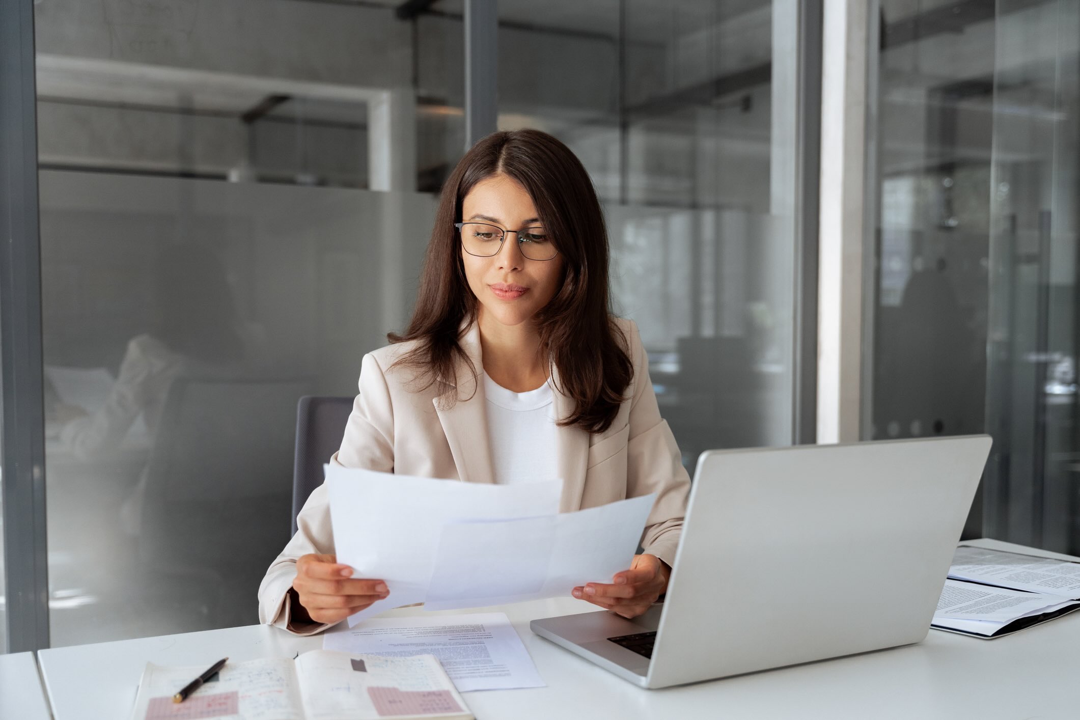Professional business woman holding papers and sitting at her laptop
