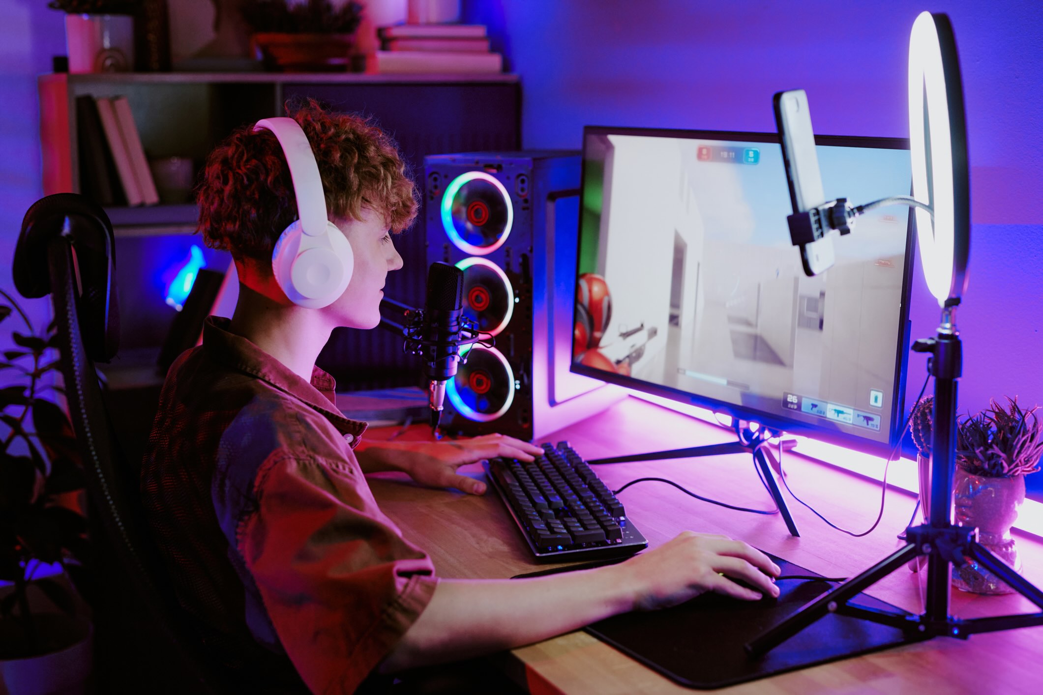 College student sitting at his PC gaming with headphones on and a mic in front of him
