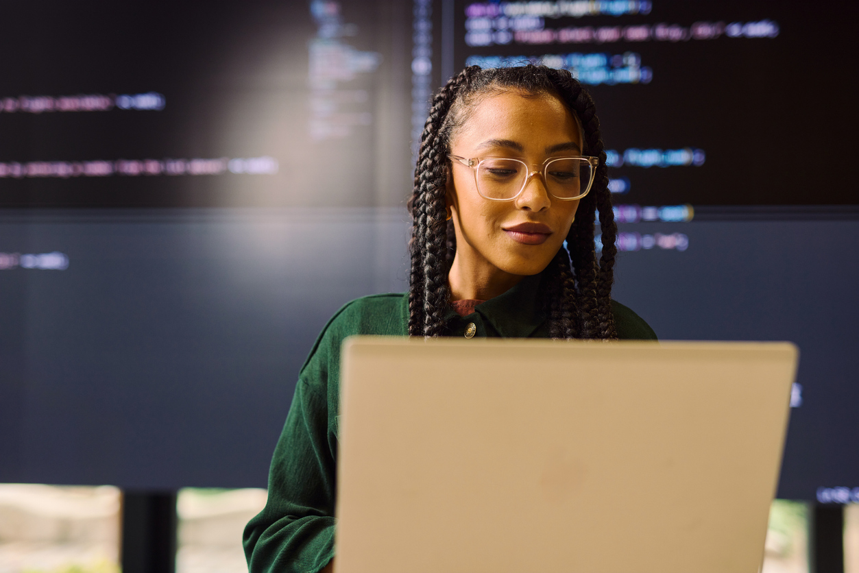 Female college student working on her laptop with screens of code behind her