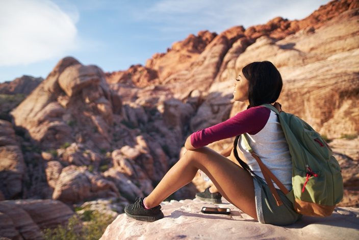 A women sitting on a cliff edge looking out into the desert and cliff landscape