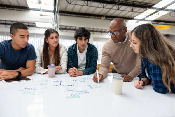 College students sitting at a white board desk with the professor drawing a diagram