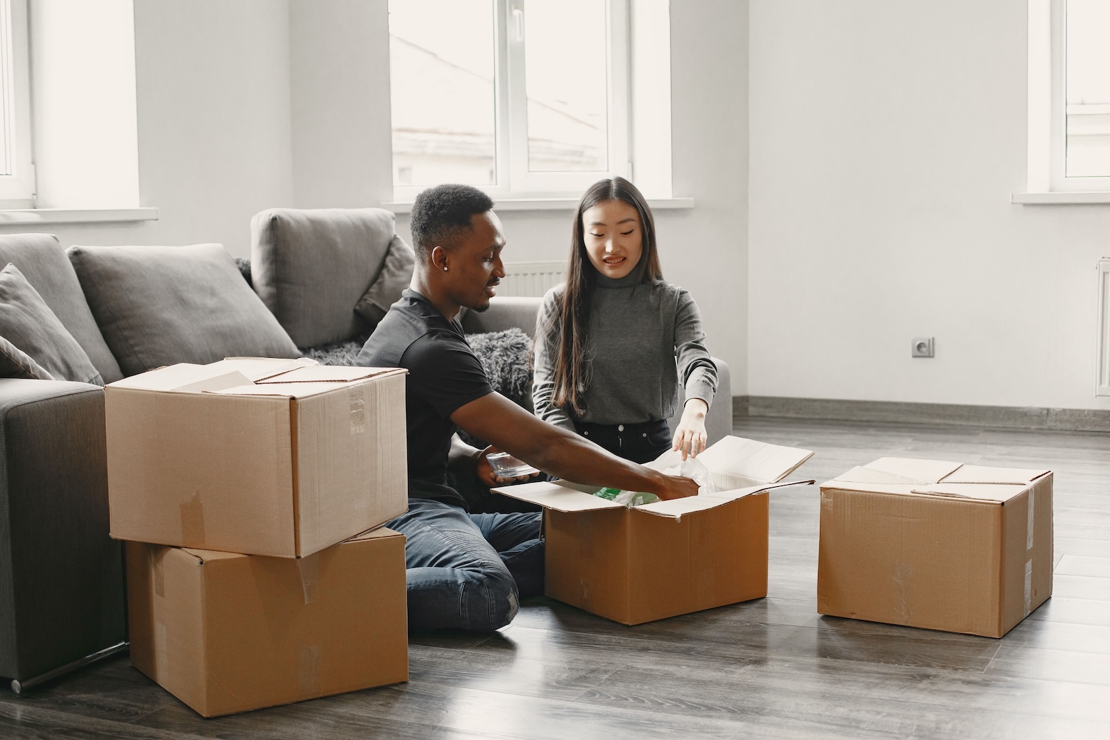 Guy and girl sitting on floor in empty apartment packing boxes