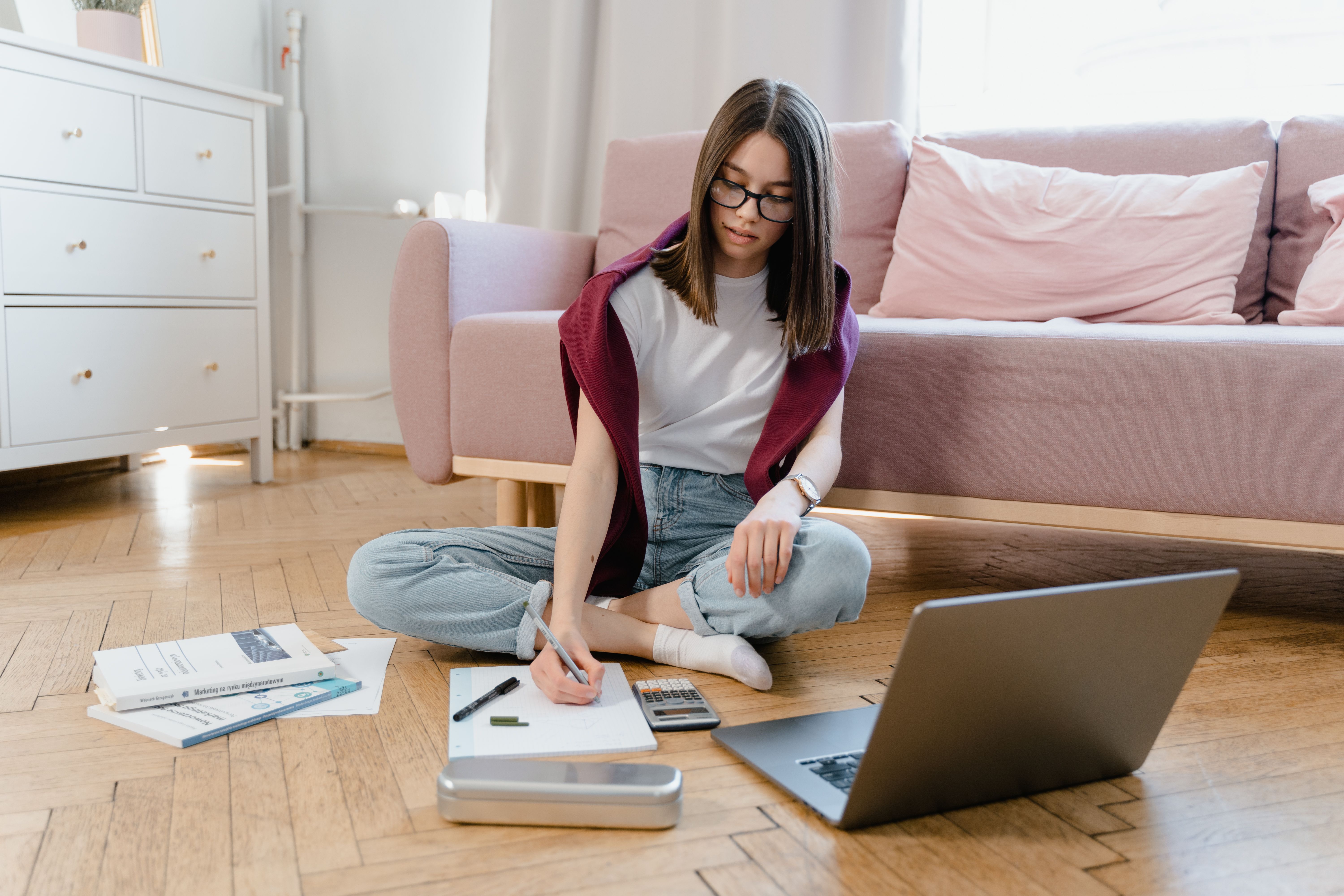 Female student sitting on the floor writing on a notebook and her laptop is open