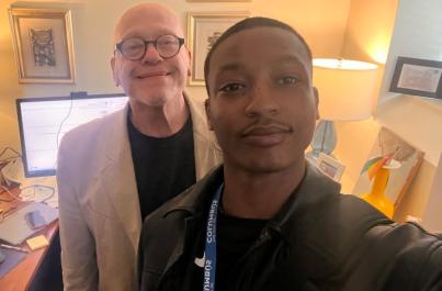 Javonte Neal and an older man smile together for a selfie in a warmly lit office, with framed artwork and a desk visible in the background.
