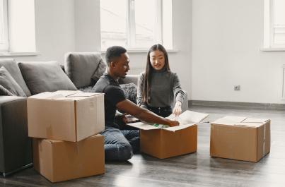 Guy and girl sitting on floor in empty apartment packing boxes