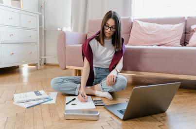 Female student sitting on the floor writing on a notebook and her laptop is open