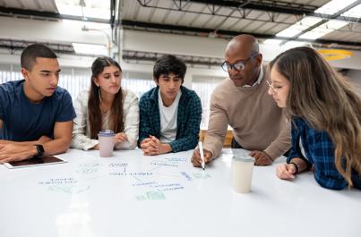 College students sitting at a white board desk with the professor drawing a diagram