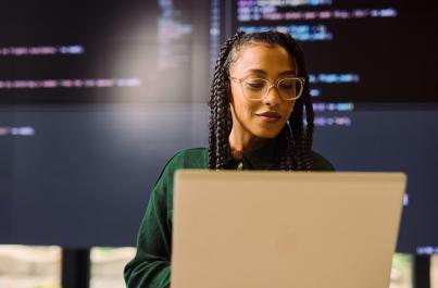 Female college student working on her laptop with screens of code behind her
