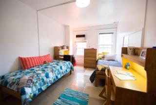 A double occupancy room with desks and a window ac unit.